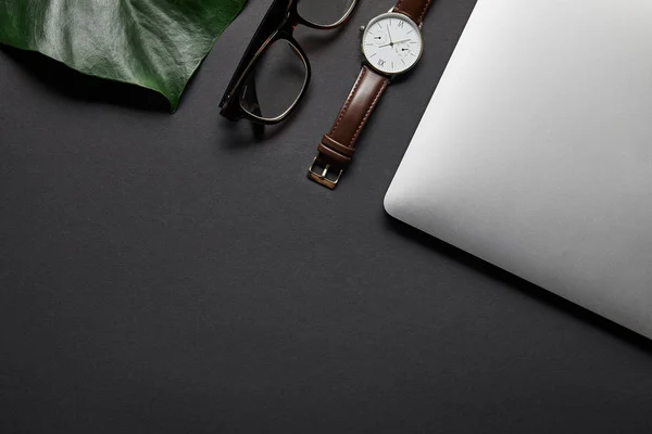 Ordinateur portable avec des lunettes et regarder sur fond noir avec feuille verte — Photo de stock