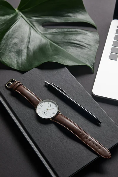 Notebook with pen and watch by laptop on black background — Stock Photo