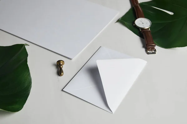 Sobre en blanco y ver sobre fondo de mármol blanco con hojas verdes - foto de stock