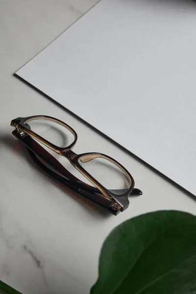 Gafas y papel en blanco sobre fondo de mármol blanco con hoja verde — Stock Photo