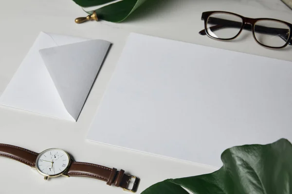 Briefvorlage mit Brille und Uhr auf weißem Marmorhintergrund mit Monstera-Blättern — Stockfoto