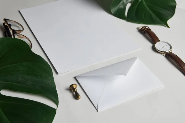 Business mock up conjunto com envelope e assistir em fundo de mármore branco com folhas monstera — Fotografia de Stock