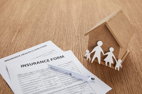 Vista de cerca del formulario de seguro, formulario de reclamo de salud del seguro, pluma, casa pequeña y familia de corte de papel en la mesa de madera - foto de stock