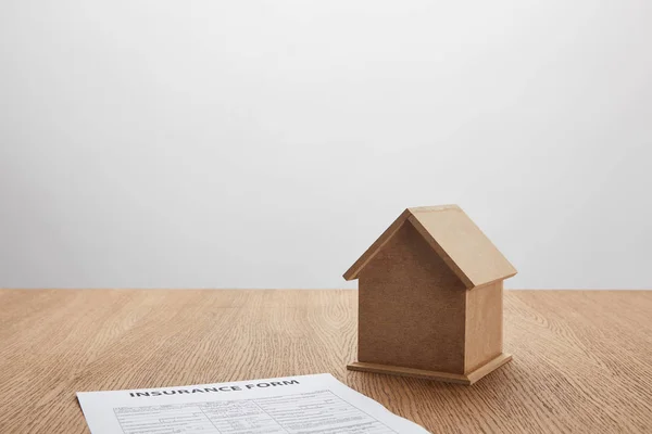 Nahaufnahme des Versicherungsformulars und des kleinen Hausmodells auf Holztisch auf grau — Stockfoto