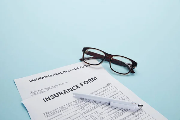 Vue rapprochée du formulaire d'assurance, du formulaire de demande de règlement d'assurance maladie, des lunettes et du stylo sur bleu — Photo de stock