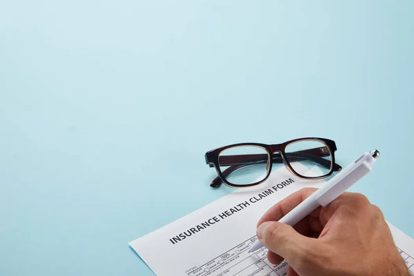 Plan recadré de la personne signant le formulaire de demande d'assurance maladie sur bleu — Photo de stock