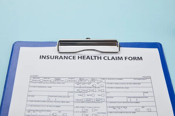 Vue rapprochée du formulaire de demande de règlement d'assurance maladie sur presse-papiers isolé sur bleu — Photo de stock