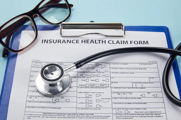 Close-up view of insurance health claim form, clipboard, eyeglasses and stethoscope on blue — Stock Photo