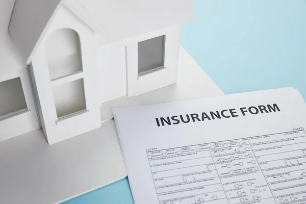 Vue rapprochée du formulaire d'assurance et du modèle de petite maison sur bleu — Photo de stock