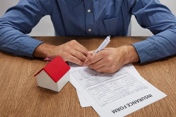 Cropped shot of man signing insurance form at wooden table with house model — Stock Photo