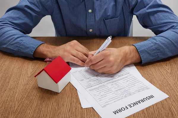 Ritagliato colpo di uomo firma modulo di assicurazione a tavolo in legno con modello di casa — Foto stock