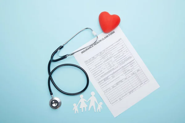 Vista superior del estetoscopio, formulario de solicitud de seguro de salud, símbolo rojo del corazón y la familia de corte de papel aislado en azul - foto de stock