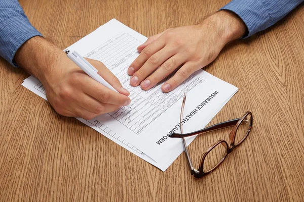 Close-up partial view of person signing insurance form at wooden table — Stock Photo