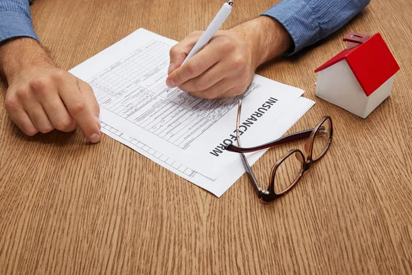 Recortado tiro de persona firma formulario de seguro en la mesa de madera - foto de stock