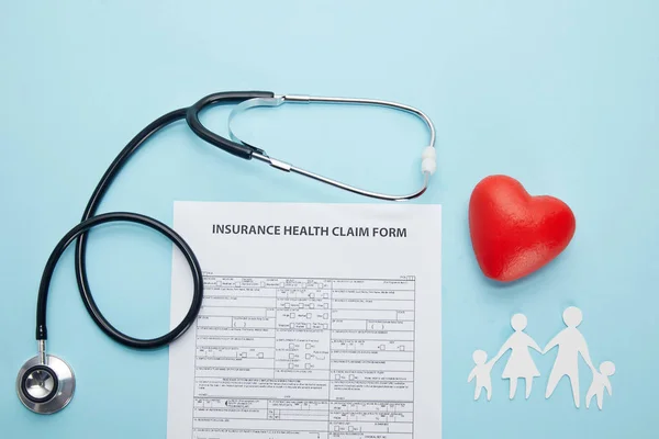 Top view of insurance health claim form, paper cut family, red heart symbol and stethoscope on blue — Stock Photo