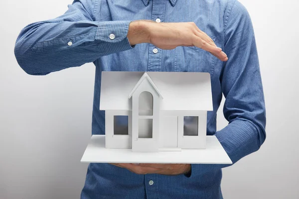 Tiro cortado de homem segurando modelo de casa pequena em cinza, conceito de seguro — Fotografia de Stock
