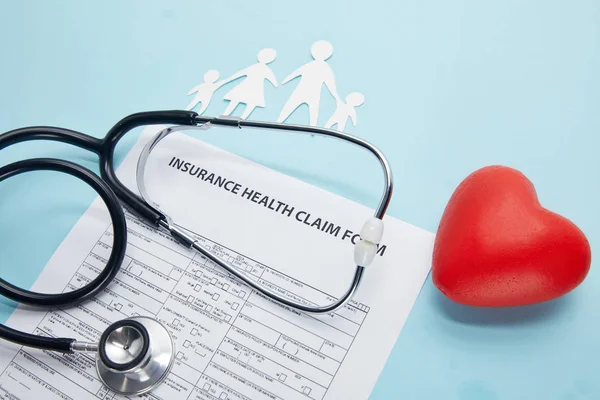 Vista de cerca del formulario de reclamo de salud del seguro, familia de corte de papel, símbolo rojo del corazón y estetoscopio en azul — Stock Photo