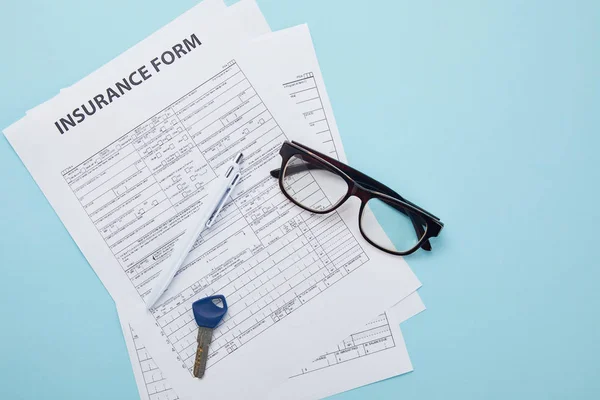 Vista superior del formulario de seguro, anteojos, llave y bolígrafo aislados en azul - foto de stock