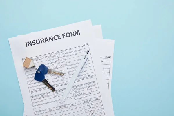 Vista superior del formulario de seguro, llaves y bolígrafo aislados en azul - foto de stock