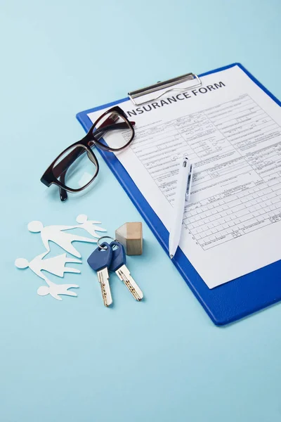 Close-up vista da forma de seguro, caneta, família de corte de papel e chaves isoladas em azul — Fotografia de Stock