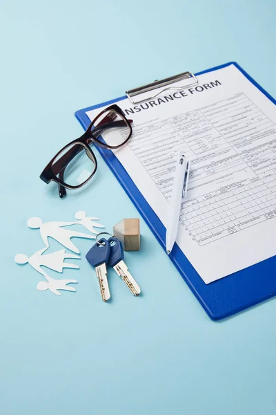 Vista de cerca del formulario de seguro, la pluma, la familia de papel cortado y las llaves aisladas en azul - foto de stock