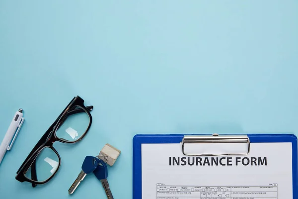 Vue rapprochée du formulaire d'assurance, des lunettes, du stylo et des clés isolés sur bleu — Photo de stock