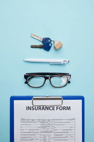 Vista superior del formulario de seguro, anteojos, bolígrafo y llaves aislados en azul - foto de stock