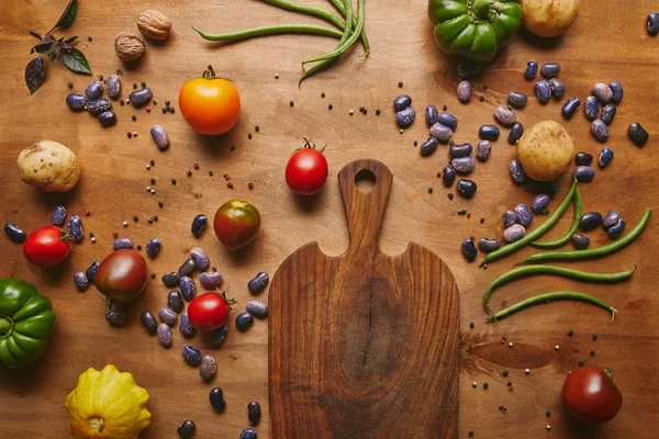 Tabla de cortar con frijoles y verduras en mesa de madera - foto de stock