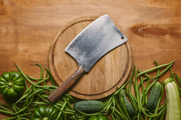 Metal cleaver on cutting board with green vegetables on wooden table — Stock Photo