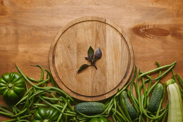 Organic raw green vegetables with round board on wooden table — Stock Photo