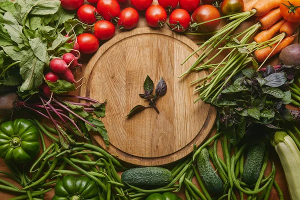 Variety of fresh vegetables and herbs by cutting board on wooden table — Stock Photo