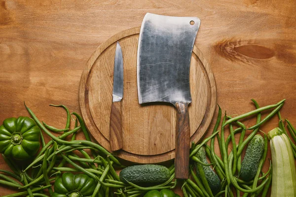 Mannaia e coltello più piccolo sul tagliere con verdure verdi sul tavolo di legno — Foto stock