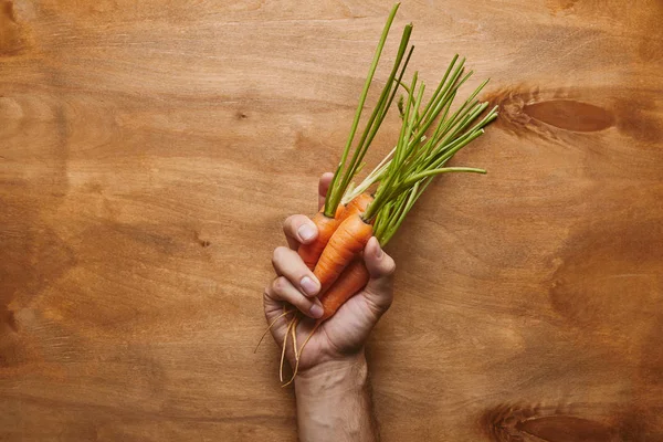 Male hand with organic carrots on wooden table — Stock Photo