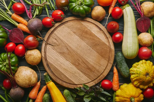 Variedad de verduras de colores por tabla de cortar en mesa de madera oscura - foto de stock
