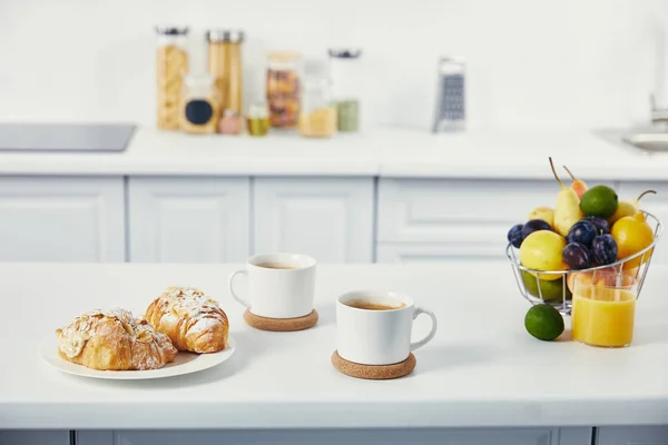 Close up view of cups of coffee and croissants for breakfast on white tabletop in kitchen — Stock Photo