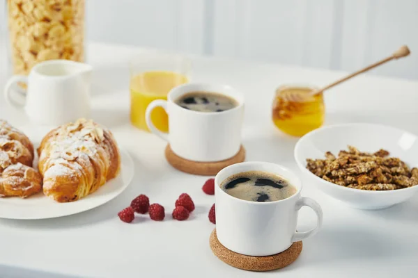 Primer plano vista de las tazas de café, croissants y frambuesas para el desayuno en la superficie blanca - foto de stock