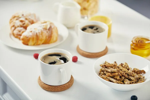 Vue rapprochée des tasses de café, croissants et framboises pour le petit déjeuner sur surface blanche — Photo de stock