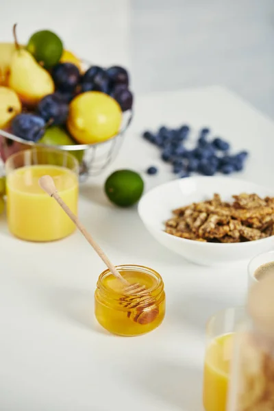 Vista ravvicinata di miele, frutta fresca e bicchiere di succo di frutta per colazione su superficie bianca — Foto stock