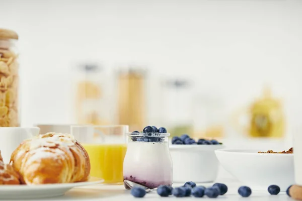Vista da vicino di yogurt sano con mirtilli freschi e croissant per la colazione su un tavolo bianco — Foto stock