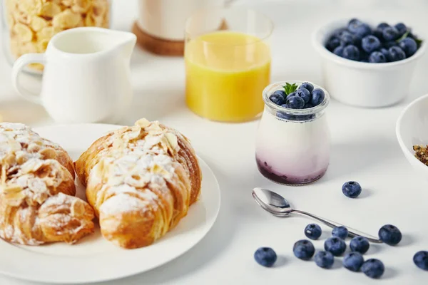 Vista de perto de iogurte saudável com mirtilos frescos e croissants para o café da manhã em mesa branca — Fotografia de Stock