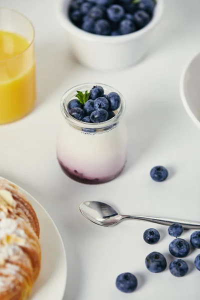 Vista de cerca del yogur saludable con arándanos frescos para el desayuno en la mesa blanca - foto de stock