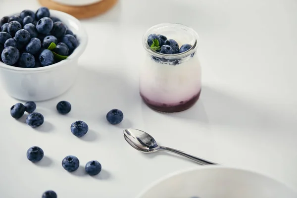 Vista ravvicinata di mirtilli freschi e yogurt per colazione su un tavolo bianco con cucchiaio — Stock Photo