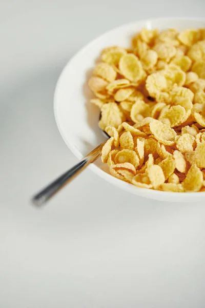 Cerrar la vista de cuchara y copos de maíz con leche en tazón para el desayuno en la superficie blanca - foto de stock