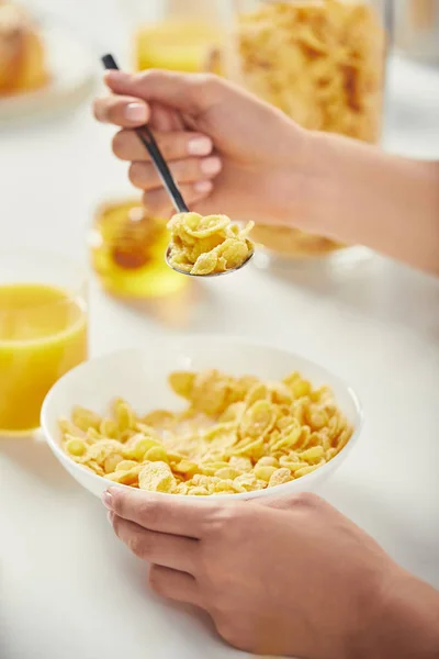 Partial view of woman with spoon sitting at table with corn flakes and glass of juice for breakfast — Stock Photo