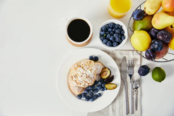 Vista superior de croissant, taza de café y vaso de jugo para el desayuno en la superficie blanca - foto de stock