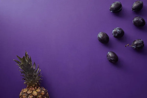 Vista dall'alto di ananas e prugne sulla superficie viola — Foto stock