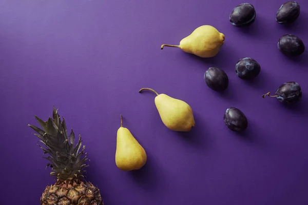 Top view of pears, plums and pineapple on violet surface — Stock Photo