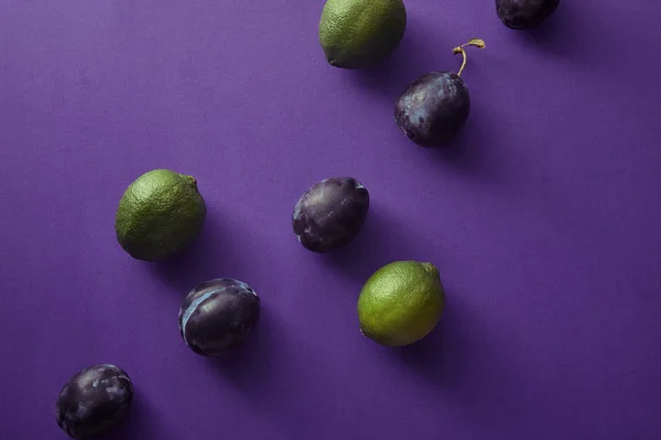 Vue de dessus des prunes et des chaux sur la surface violette — Photo de stock