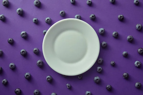 Vista dall'alto di piastra e mirtilli su superficie viola — Foto stock