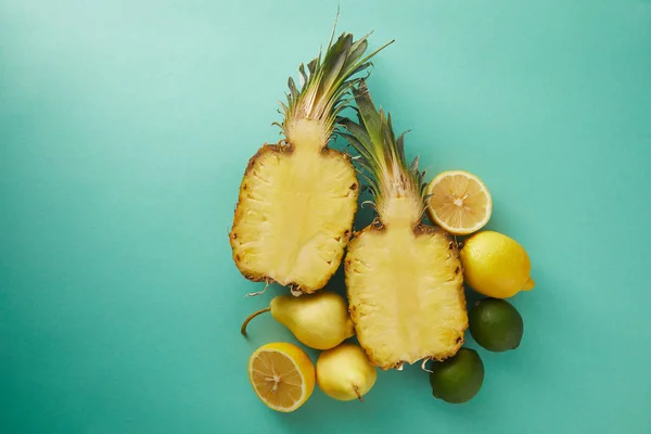 Vista elevata di ananas, pere e limoni tagliati su superficie turchese — Foto stock
